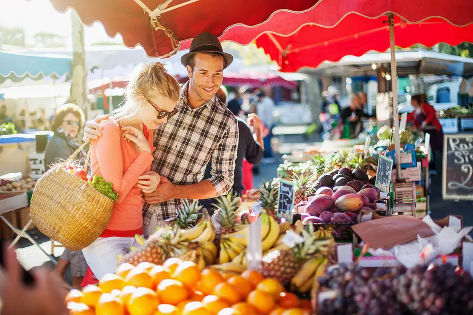 Couple faisant ses courses devant un étal de fruits et légumes au marché